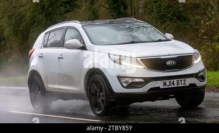 Milton Keynes, Bucks, Regno Unito - 9 dicembre 2023: SUV Kia Sportage con motore diesel bianco del 2014 che guida su una strada bagnata, sotto la pioggia con i fari accesi Foto Stock
