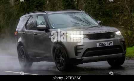 Milton Keynes, Bucks, Regno Unito - 9 dicembre 2023: Land Rover Discovery con motore diesel argento 2017 che guida su una strada bagnata, sotto la pioggia con i fari accesi Foto Stock