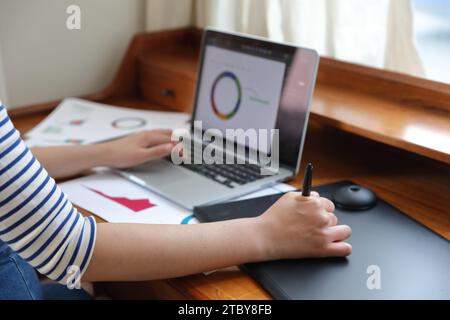 Donna che disegna grafici e grafici utilizzando tablet e notebook Foto Stock
