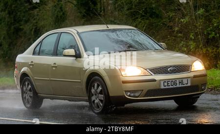 Milton Keynes,Bucks,Regno Unito - 13 dicembre 2023: Auto Ford Mondeo dorata del 2006 che guida su una strada bagnata, sotto la pioggia con i fari accesi Foto Stock