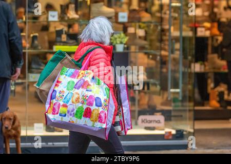 Donna che trasporta diverse borse per la spesa natalizia multicolore riutilizzabili a Preston, Regno Unito. 8 dicembre 2023. Negozi natalizi, negozi, shopping in una giornata umida a Fishergate High Street. Credito ; MediaWorldImages/AlamyLiveNews Foto Stock