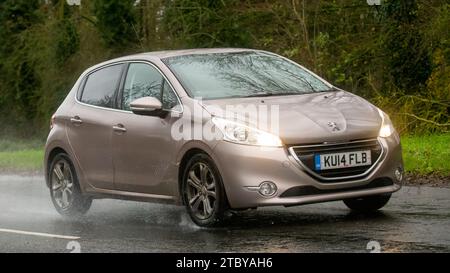 Milton Keynes,Bucks,Regno Unito - 13 dicembre 2023: 2014 Peugeot rosa 208 guida su una strada bagnata, sotto la pioggia con i fari accesi Foto Stock