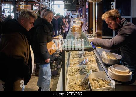 MADRID SPAGNA - 09 DICEMBRE 2023: Chiosco di ostriche fresche al mercato di San Miguel a Madrid, Spagna. La gente si riunisce intorno al banco, guardando gli selecti Foto Stock