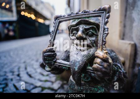 Wrocław, polonia - 8 dicembre 2023: L'iconico nano Wrocław di nome Galeriusz si trova su un marciapiede che regge una cornice di pittura Foto Stock