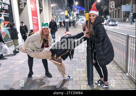 Broad Street, Birmingham 9 dicembre 2023 - i venditori hanno lottato per rimanere in posizione eretta sabato sera mentre raffiche di vento fino a 50 km/h colpivano Birmingham mentre Storm Elin colpiva la regione. I festaioli si sono rovinati i capelli, dato che gli edifici hanno creato un effetto tunnel del vento. La maggior parte indossava cappotti caldi e sciarpe, ma alcuni venivano fuori in abiti da festa, pronti a ballare tutta la notte, qualunque fosse il tempo all'aperto. I salti e i cappelli di Babbo Natale sono stati il tema della serata mentre la stagione delle feste di Natale è iniziata. Credito: Stop Press Media/Alamy Live News Foto Stock