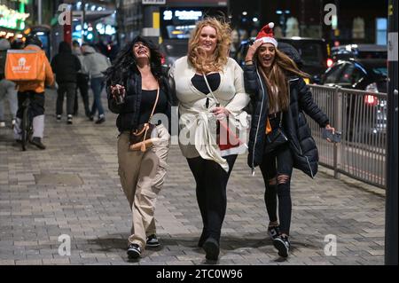 Broad Street, Birmingham 9 dicembre 2023 - i venditori hanno lottato per rimanere in posizione eretta sabato sera mentre raffiche di vento fino a 50 km/h colpivano Birmingham mentre Storm Elin colpiva la regione. I festaioli si sono rovinati i capelli, dato che gli edifici hanno creato un effetto tunnel del vento. La maggior parte indossava cappotti caldi e sciarpe, ma alcuni venivano fuori in abiti da festa, pronti a ballare tutta la notte, qualunque fosse il tempo all'aperto. I salti e i cappelli di Babbo Natale sono stati il tema della serata mentre la stagione delle feste di Natale è iniziata. Credito: Stop Press Media/Alamy Live News Foto Stock