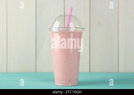 Frullato gustoso in tazza di plastica su un tavolo azzurro contro una parete di legno bianco Foto Stock