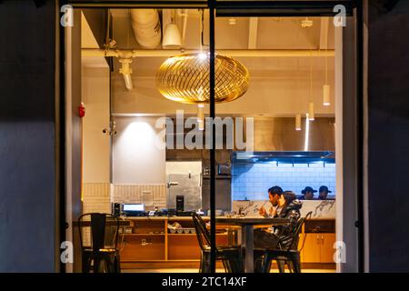 Ristorante informale di sera con una giovane coppia che mangia a un tavolo e due cuochi dietro il bancone Foto Stock