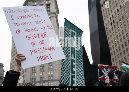 New York, Stati Uniti. 8 dicembre 2023. Un manifestante tiene un cartello che dice: "Chi condanni? Condanno lo Stato terroristico di Israele per il GENOCIDIO DEL POPOLO PALESTINESE”. I manifestanti pro-Palestina marciano per protestare contro le compagnie americane e statunitensi per il loro sostegno a Israele durante il conflitto israelo-palestinese. La manifestazione è proseguita oltre Wall Stret dopo che gli Stati Uniti hanno posto il veto al progetto di risoluzione del Consiglio di sicurezza delle Nazioni Unite che chiede un immediato cessate il fuoco hanno raggiunto gli organizzatori. Credito: SOPA Images Limited/Alamy Live News Foto Stock