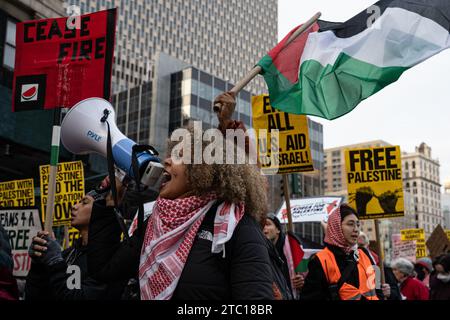 New York, Stati Uniti. 8 dicembre 2023. Un organizzatore canta in un megafono. I manifestanti pro-Palestina marciano per protestare contro le compagnie americane e statunitensi per il loro sostegno a Israele durante il conflitto israelo-palestinese. La manifestazione è proseguita oltre Wall Stret dopo che gli Stati Uniti hanno posto il veto al progetto di risoluzione del Consiglio di sicurezza delle Nazioni Unite che chiede un immediato cessate il fuoco hanno raggiunto gli organizzatori. Credito: SOPA Images Limited/Alamy Live News Foto Stock