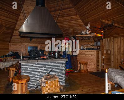 Saariselka, Finlandia - 29 novembre 2010: Una donna sami in abito tradizionale sta cucinando in un "kota" usato per ospitare una cena per i turisti. Il kota ( Foto Stock