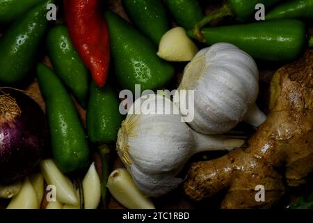 Aglio fresco, cipolla, freddo verde, pollo crudo, zenzero, foglie di coriandolo e foglie di curry su vassoio di legno con acqua cosparsa su quelle verdure. Foto Stock