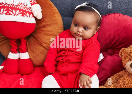 Bambino afro-americano sorridente seduto sul divano con la bambola di babbo natale a casa Foto Stock