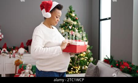 Giovane donna incinta che festeggia il natale, disimballando il regalo a casa Foto Stock