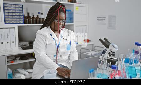 Scienziata afroamericana concentrata impegnata in una seria ricerca medica sul suo portatile in laboratorio, ritratto di un bellissimo adulto con trecce consegnare Foto Stock