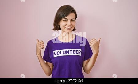 Giovane donna ispanica entusiasta, volontaria lampeggia con un gesto sicuro del pollice, sfoggia capelli corti e uniforme di beneficenza, isolando orecchio-orecchio Foto Stock