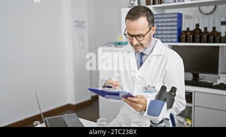 Un uomo serio di mezza età, scienziato dei capelli grigi, che prende appunti intensamente negli appunti del suo laboratorio di lavoro. coscienziosamente immerso nella ricerca medica con un Foto Stock