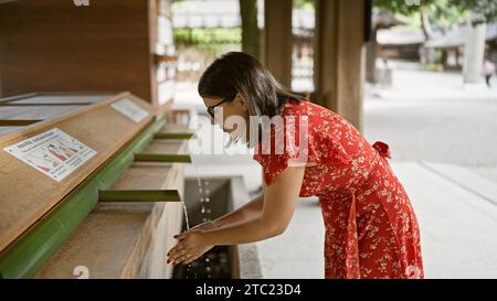 La bella donna ispanica con gli occhiali partecipa al tradizionale rituale purificante asiatico al tempio meiji, lavandosi le mani in acqua naturale fluente da Foto Stock