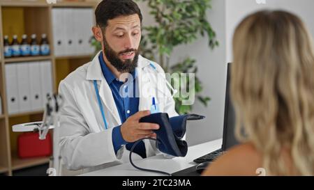 Giovane medico ispanico che misura il polso del paziente utilizzando il tensiometro a braccio presso la clinica Foto Stock