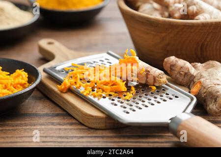 Radici di curcuma fresche grattugiate e grattugia. Ciotole di radici di curcuma intere e grattugiate, polvere di curcuma sullo sfondo. Cibo sano. Foto Stock
