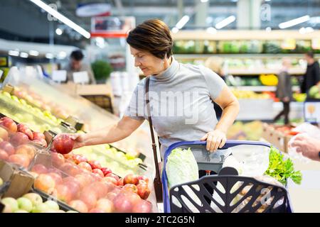 Donna positiva sceglie le mele rosse mature sulla finestra del negozio di alimentari Foto Stock