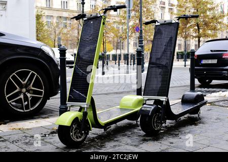 Moderni scooter elettrici per città alimentati a fotovoltaico sul marciapiede di pietra in zona urbana in inverno. pannelli fotovoltaici di grandi dimensioni collegati. trasporto ecologico. Foto Stock