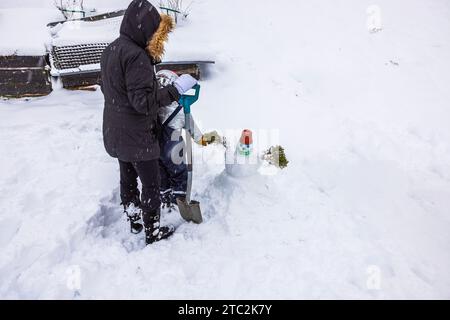 Veduta di donna e bambino che scompongono gioiosamente il pupazzo di neve nel loro cortile. Svezia. Foto Stock