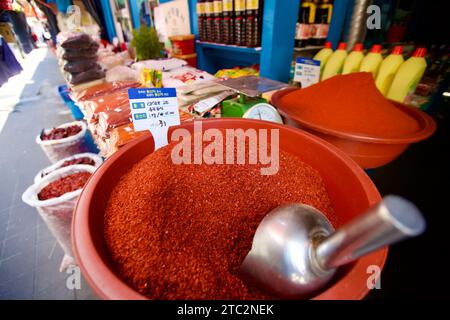 Una ciotola piena di peperoni rossi finemente macinati cattura l'essenza dei sapori tradizionali coreani, presentata in un vivace ambiente di mercato. Foto Stock