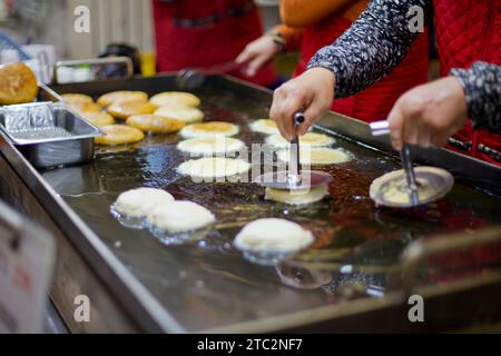 Una donna spinge sapientemente la pastella Hotteok in olio frizzante in un tradizionale mercato coreano, mostrando l'arte di preparare questo amato cibo di strada. Foto Stock