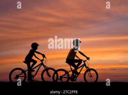 silhouette di due ragazze in bicicletta sullo sfondo del cielo al tramonto Foto Stock