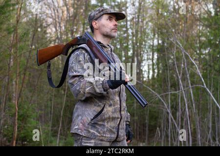 Un cacciatore tiene un fucile scaricato sulla spalla la sera in una radura forestale. Foto Stock