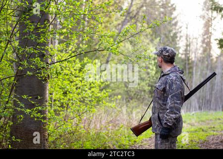 un cacciatore con un fucile sulla spalla guarda indietro in primavera alla radura di una foresta Foto Stock