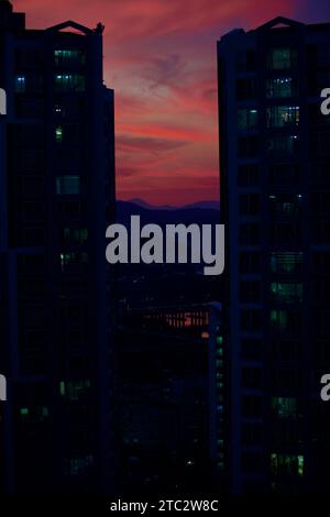 Lo skyline di Ulsan al tramonto, con le sue oscure sagome di appartamenti, il cielo vibrante, il tranquillo fiume Taehwa e l'iconico ponte Taehwa. Foto Stock