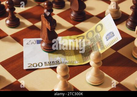 Soldi in euro con pezzi di re scacchi sulla scacchiera, primo piano. Foto Stock