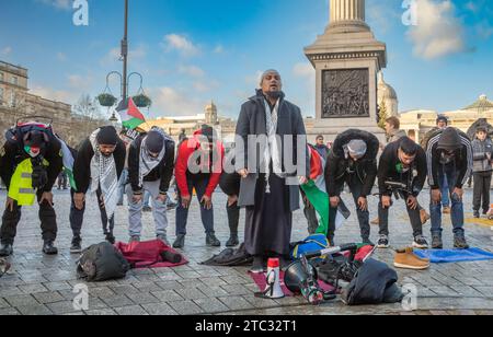 Londra / Regno Unito - 9 dicembre 2023: Un gruppo di uomini musulmani pregano a Trafalgar Square in una manifestazione pro-palestinese che chiede la fine degli attacchi israeliani contro G. Foto Stock