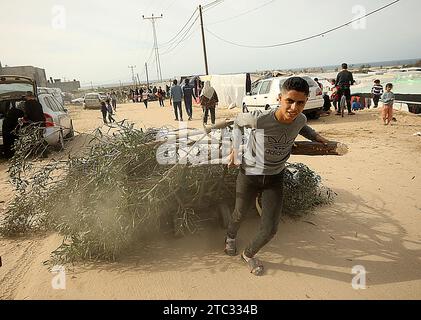 Khan Yunis, Gaza. 9 dicembre 2023. Un ragazzo palestinese che trascina legna da ardere per i camini mentre cammina davanti a tende erette da palestinesi sfollati da intensi bombardamenti israeliani sulla Striscia di Gaza in aree aperte vicino al confine egiziano a Rafah, nel sud dell'enclave palestinese, domenica 10 dicembre 2023., mentre i palestinesi ricorrono alle alternative più economiche disponibili per cucinare e riscaldare in mezzo a una scarsità di risorse mentre continuano le battaglie tra Israele e i militanti palestinesi nella striscia di Gaza. Foto di Ismael Mohamad/UPI. Crediti: UPI/Alamy Live News Foto Stock