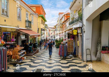 Una strada trafficata di negozi e caffetterie marciapiedi con tradizionali piastrelle a mosaico Calcada nella città vecchia della città costiera di Cascais, in Portogallo. Foto Stock