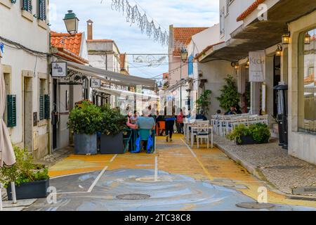 Una strada trafficata di negozi e caffetterie marciapiedi con tradizionali piastrelle a mosaico Calcada nella città vecchia della città costiera di Cascais, in Portogallo. Foto Stock