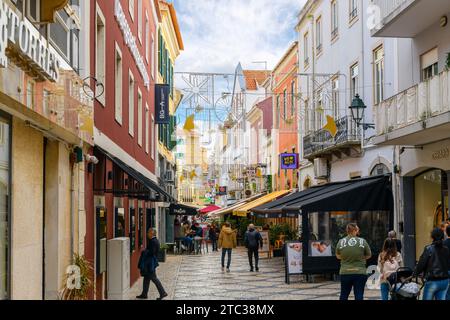 Una strada trafficata di negozi e caffetterie marciapiedi con tradizionali piastrelle a mosaico Calcada nella città vecchia della città costiera di Cascais, in Portogallo. Foto Stock