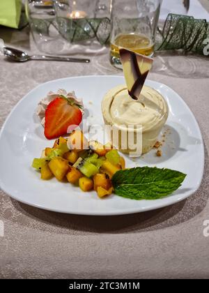 Dessert su un piatto composto da una fragola, frutta, foglia di menta e un gelato a base di purea di castagne. Foto Stock