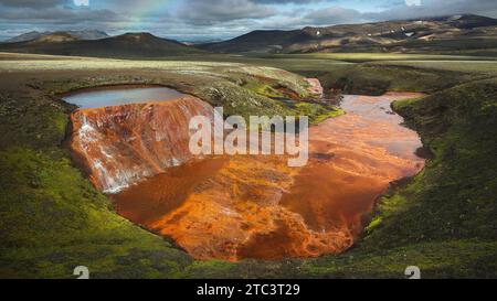 Un ruscello poco profondo che si snoda attraverso un paesaggio arido soleggiato, con macchie di lussureggiante erba verde sparse ovunque Foto Stock