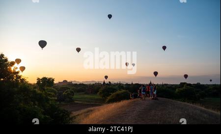 Un grande gruppo di persone si trova sullo sfondo, guardando in alto con meraviglia le colorate mongolfiere che si innalzano sopra di loro nel cielo soleggiato Foto Stock