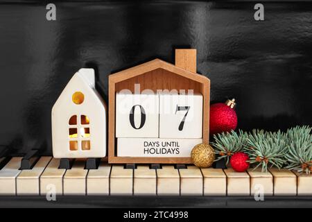 Calendario con testo 7 GIORNI FINO ALLE FESTIVITÀ e decorazioni natalizie sulle chiavi del pianoforte Foto Stock