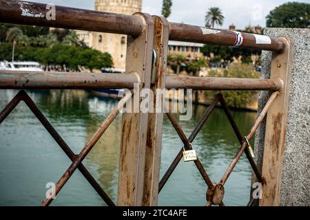 Una vista ravvicinata delle serrature d'amore attaccate a una ringhiera arrugginita con Torre del Oro, Siviglia, Spagna, sullo sfondo. Foto Stock