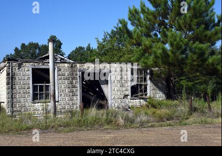 Il vecchio negozio di campagna è derelict e siede in rovina. Il palo di metallo di segno sta davanti al deposito dove la pompa del gas ha seduto. Il tetto è stato scavato. Foto Stock