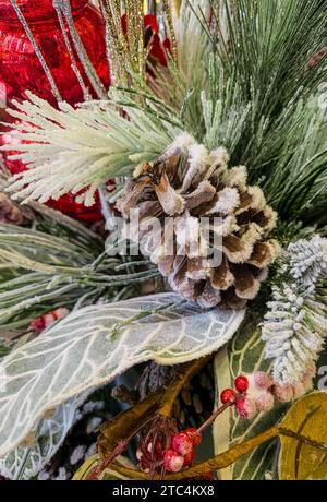 Foto di sfondo del pinecone invernale e dei bocchi di pini ricoperti di neve con ornamenti rossi e bacche di holly Foto Stock