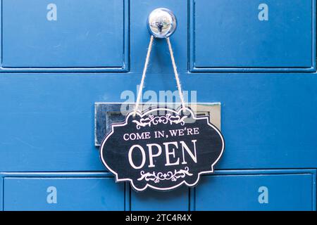 L'iscrizione su un cartello nero su una porta blu - entra, siamo aperti Foto Stock