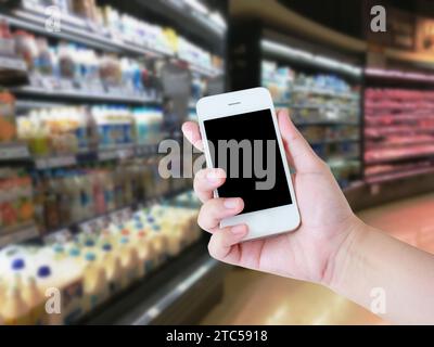 telefono cellulare con mano con yogurt, latte di soia e latte sugli scaffali di un supermercato Foto Stock