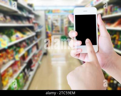 Dispositivo mobile che tiene la mano con sfocatura degli scaffali dei supermercati sullo sfondo, concetto di shopping online. Foto Stock