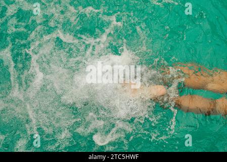 Gambe da uomo in piscina. Foto dall'alto della parte inferiore del corpo dell'uomo che nuota nell'acqua blu. Piedi che spruzzano nella piscina. Vacanza e. Foto Stock